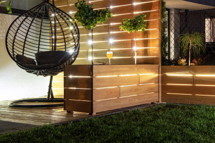 Residential Backyard Garden Wooden Recreation Place Deck with Table Illuminated by LED Outdoor Lighting. Custom Made Wooden Element.